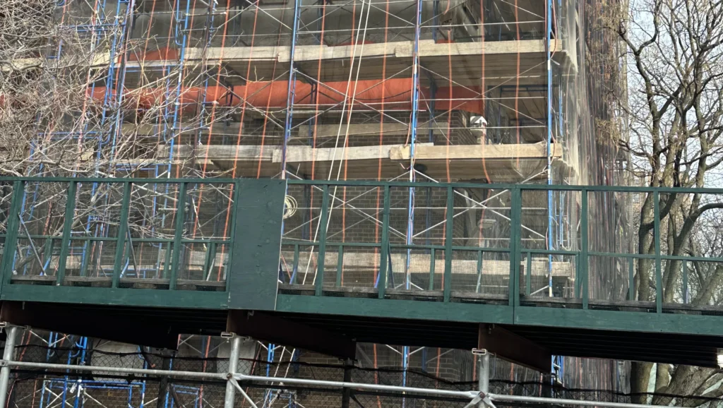 Pedestrian walkway covered with a sidewalk shed in Rockville Centre during a public festival, maintaining safety near construction activity